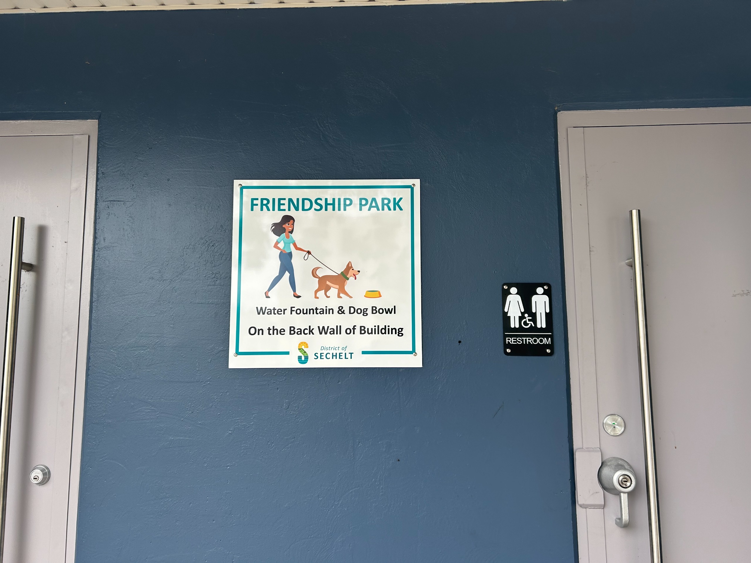 Sign on door that reads water fountain and dog bowl on the back wall of the building